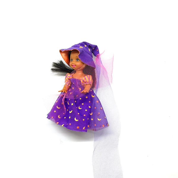 A vintage 2003 Mattel Barbie Kelly Club Halloween Party Deidre as a Witch mini doll. The doll features brown hair and is wearing a purple dress and matching pointed witch hat decorated with gold metallic stars and crescent moons, accented by a purple mesh veil. Isolated on a solid white background