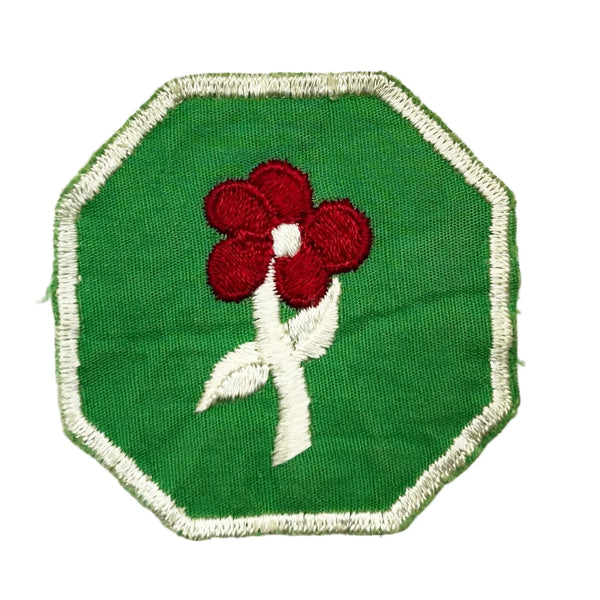 This is a vintage Girl Scout troop crest patch, featuring a red flower design with a white center and stem on a green octagonal background. This specific design has been retired. It depicts either a Scarlet Pimpernel or a Cardinal Flower, with the specific name depending on the era it was produced.