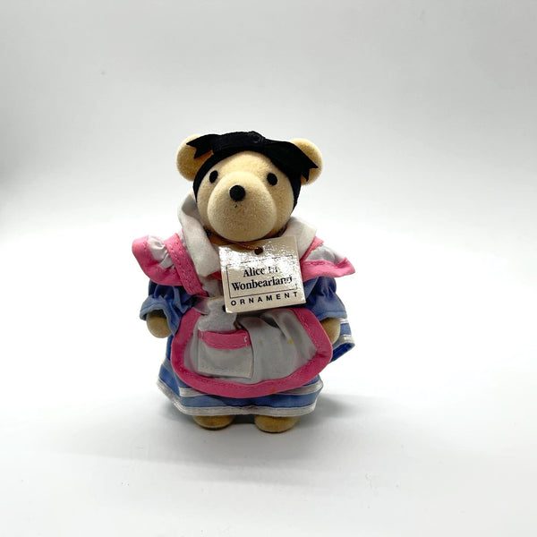A small plush teddy bear ornament dressed in a white apron with pink trim and blue sleeves, wearing a black bow. 
