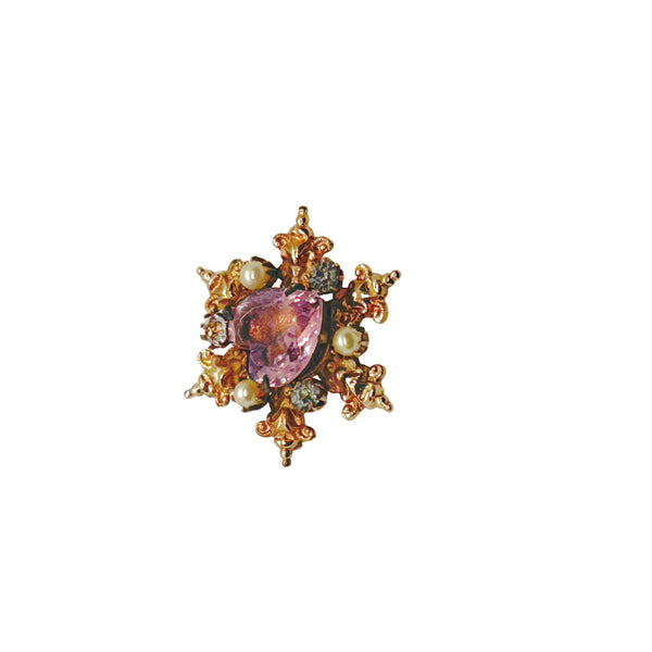 A gold-toned brooch with a central heart-shaped, light purple gemstone. The brooch is surrounded by ornate gold filigree, small pearls, and clear crystals, creating a vintage, elegant design.