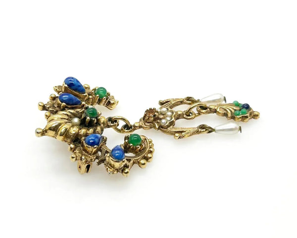 A splendid specimen of Renaissance Revival style, this Vintage ART Brooch showcases the maker's hallmark artistry through its exquisite detailing. Adorned with faux lapis, jade, turquoise, and pearl accents set within ornate gold-tone metalwork, it presents a harmonious marriage of color and design.