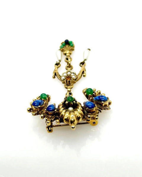 A splendid specimen of Renaissance Revival style, this Vintage ART Brooch showcases the maker's hallmark artistry through its exquisite detailing. Adorned with faux lapis, jade, turquoise, and pearl accents set within ornate gold-tone metalwork, it presents a harmonious marriage of color and design.
