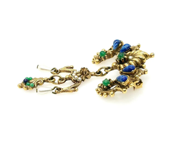 A splendid specimen of Renaissance Revival style, this Vintage ART Brooch showcases the maker's hallmark artistry through its exquisite detailing. Adorned with faux lapis, jade, turquoise, and pearl accents set within ornate gold-tone metalwork, it presents a harmonious marriage of color and design.