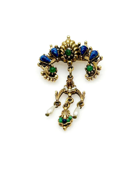 A splendid specimen of Renaissance Revival style, this Vintage ART Brooch showcases the maker's hallmark artistry through its exquisite detailing. Adorned with faux lapis, jade, turquoise, and pearl accents set within ornate gold-tone metalwork, it presents a harmonious marriage of color and design.