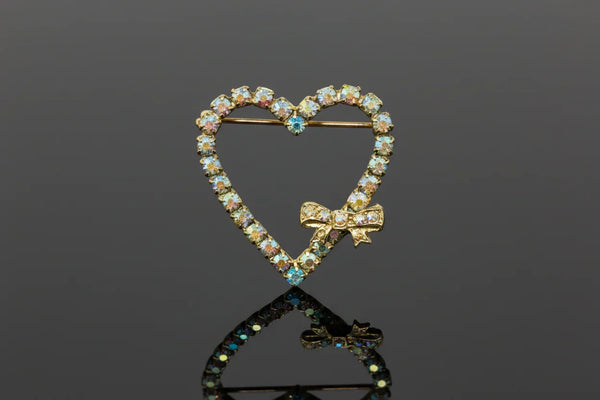 A charming mid-century treasure from the 1940s-50s, this whimsical sweetheart bow pin captures all the romance of vintage style. Crafted from early celluloid plastic, it showcases a playful "Heart Within a Heart" design—a red bow crowning a white heart outline with a dangling red heart that swings freely below.