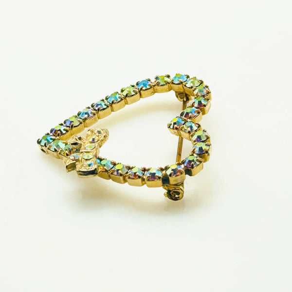 This charming mid-century brooch captures all the sparkle and romance of vintage glamour. The delicate gold-tone heart showcases shimmering aurora borealis rhinestones that dance with rainbow fire, while a sweet bow accent adds an extra touch of whimsy.