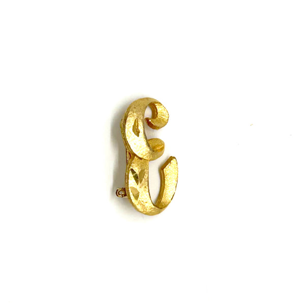 A small gold initial 'E' brooch with a textured, matte finish and a loop on the side, shown on a plain white background.