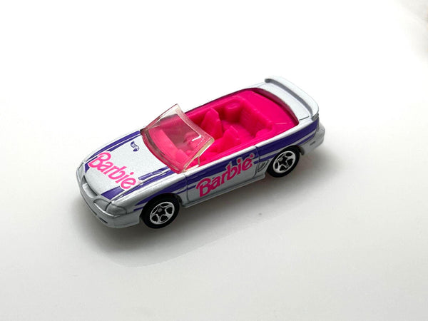 Hot Wheels Barbie 1996 Ford Mustang GT convertible, featuring a silver exterior with purple and pink branding.