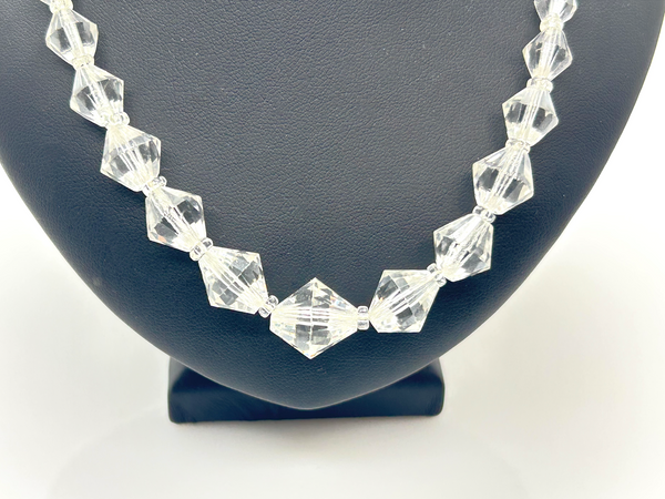 A clear faceted crystal bead necklace displayed on a black jewelry bust against a white background.