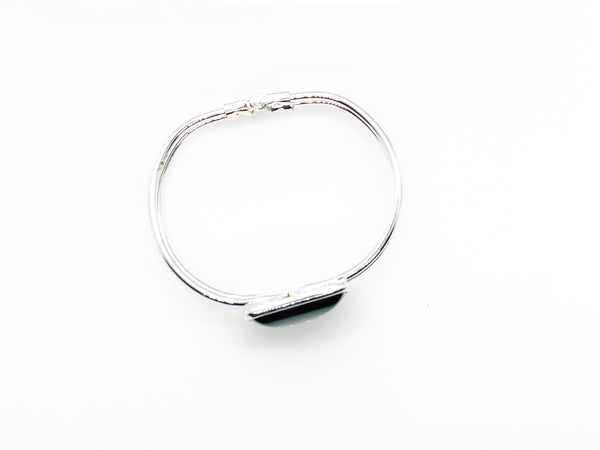 This striking vintage bracelet showcases a bold black square onyx stone set in polished silver. The architectural design features dual silver bands converging at the center stone with a hinged hook-bangle closure for easy wear. 