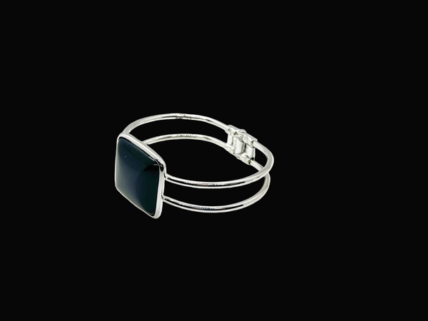 This striking vintage bracelet showcases a bold black square onyx stone set in polished silver. The architectural design features dual silver bands converging at the center stone with a hinged hook-bangle closure for easy wear. 