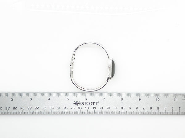 This striking vintage bracelet showcases a bold black square onyx stone set in polished silver. The architectural design features dual silver bands converging at the center stone with a hinged hook-bangle closure for easy wear. 