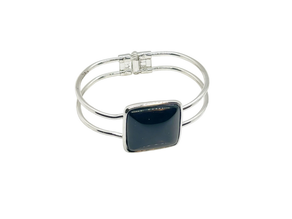 This striking vintage bracelet showcases a bold black square onyx stone set in polished silver. The architectural design features dual silver bands converging at the center stone with a hinged hook-bangle closure for easy wear. 