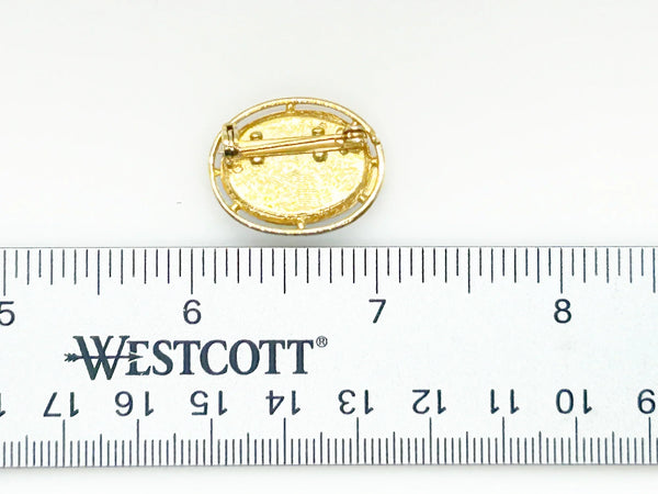 Picture a charming piece of wearable nostalgia: this oval brooch pairs a moody black canvas with cheerful painted florals, all framed in warm gold-tone metal. It's a mid-20th century take on Victorian mourning jewelry aesthetics