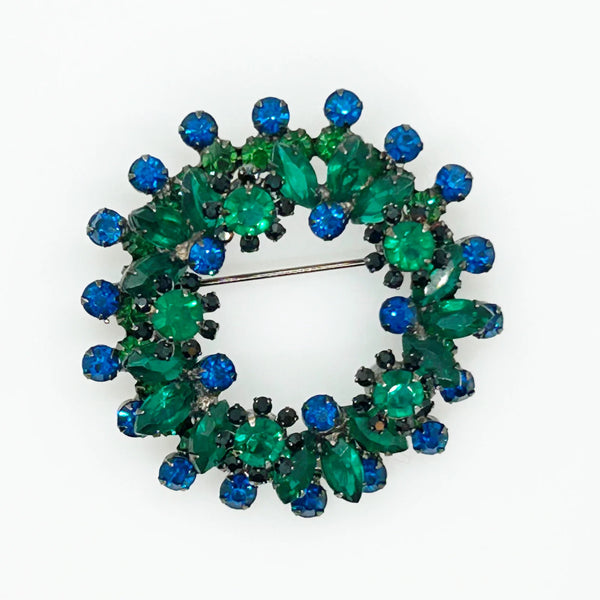 This stunning brooch features a dazzling mix of blue and green rhinestones in round and marquise cuts, all set in blackened metal for a striking layered effect. Its eye-catching design is complemented by excellent condition and the distinctive figure 8 markings on the back, suggesting it’s an unsigned Juliana piece. Measuring 2 inches wide, this unique accessory is perfect for adding vintage charm to any outfit. Enjoy Free Shipping with your purchase.