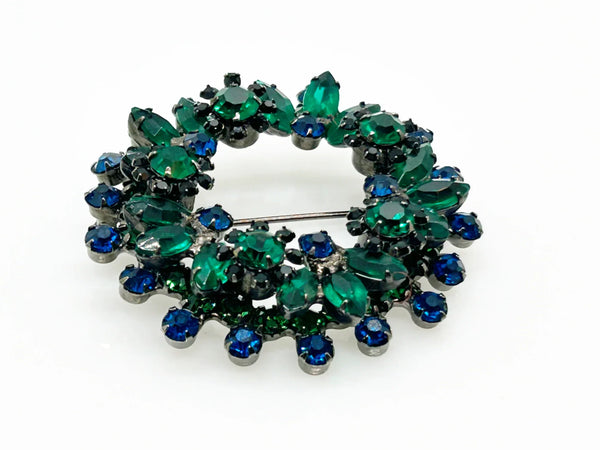 This stunning brooch features a dazzling mix of blue and green rhinestones in round and marquise cuts, all set in blackened metal for a striking layered effect. Its eye-catching design is complemented by excellent condition and the distinctive figure 8 markings on the back, suggesting it’s an unsigned Juliana piece. Measuring 2 inches wide, this unique accessory is perfect for adding vintage charm to any outfit. Enjoy Free Shipping with your purchase.