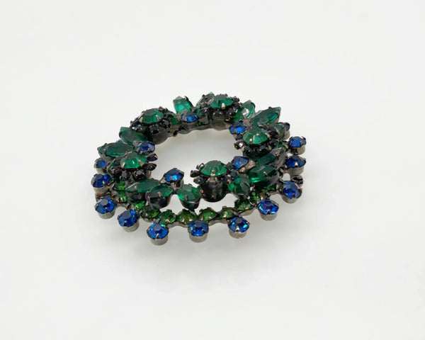 This stunning brooch features a dazzling mix of blue and green rhinestones in round and marquise cuts, all set in blackened metal for a striking layered effect. Its eye-catching design is complemented by excellent condition and the distinctive figure 8 markings on the back, suggesting it’s an unsigned Juliana piece. Measuring 2 inches wide, this unique accessory is perfect for adding vintage charm to any outfit. Enjoy Free Shipping with your purchase.