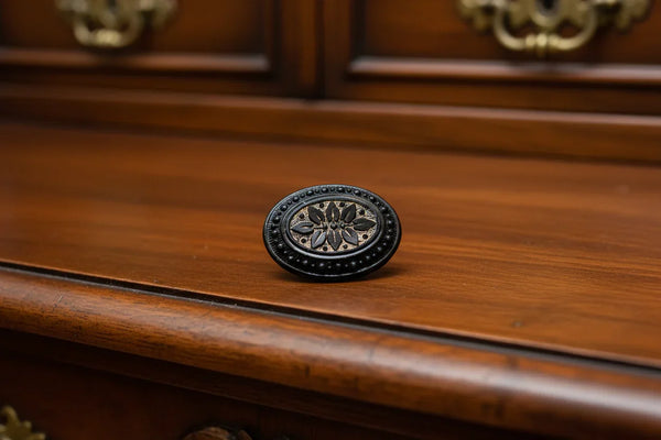 Discover this exquisite antique Victorian black glass brooch, a poignant piece of mourning jewelry originating from the mid-to-late 19th century. This captivating oval brooch boasts a delicately beaded border, framing a mesmerizing central design that evokes either a floral motif or a radiant starburst pattern. 