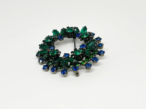 This stunning brooch features a dazzling mix of blue and green rhinestones in round and marquise cuts, all set in blackened metal for a striking layered effect. Its eye-catching design is complemented by excellent condition and the distinctive figure 8 markings on the back, suggesting it’s an unsigned Juliana piece. Measuring 2 inches wide, this unique accessory is perfect for adding vintage charm to any outfit. Enjoy Free Shipping with your purchase.