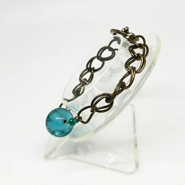 This captivating vintage bracelet boasts two rows of links on either side of a stunning blue glass marble with shimmering gold stripes. It is 7 1/2" in length and features a charming toggle clasp