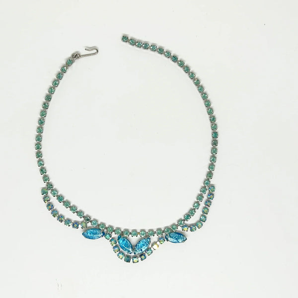 This exquisite brooch with an Old World aesthetic showcases finely crafted gold filigree petals encircling a square stone in elegant blue-purple tones. Between each delicate petal rests a round, iridescent stone that complements the central hues, adding subtle depth and shimmer.