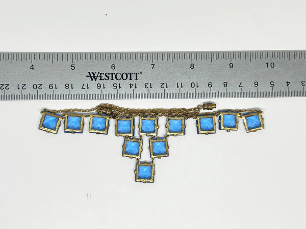 Experience the height of sophistication with this exquisite vintage Art Deco necklace. Featuring a flawless line of rich azure square stones, delicately connected by two additional rows, all set on a luxurious gold tone link chain. The stones are meticulously held in place with thin claw settings, revealing their exposed backs for an added touch of elegance.