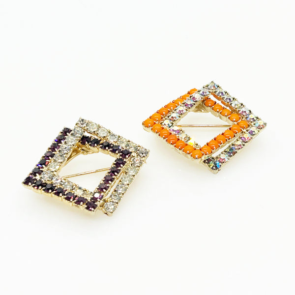 Set of two vintage 3D interlocking square brooches. One features purple and clear prong-set rhinestones on a silver-tone frame. The other features opaque orange and sparkling gold AB crystals on a gold-tone geometric frame