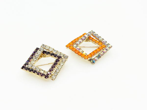 Set of two vintage 3D interlocking square brooches. One features purple and clear prong-set rhinestones on a silver-tone frame. The other features opaque orange and sparkling gold AB crystals on a gold-tone geometric frame
