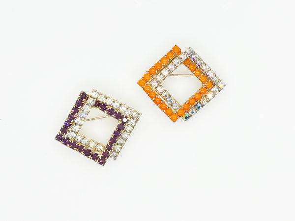 Set of two vintage 3D interlocking square brooches. One features purple and clear prong-set rhinestones on a silver-tone frame. The other features opaque orange and sparkling gold AB crystals on a gold-tone geometric frame