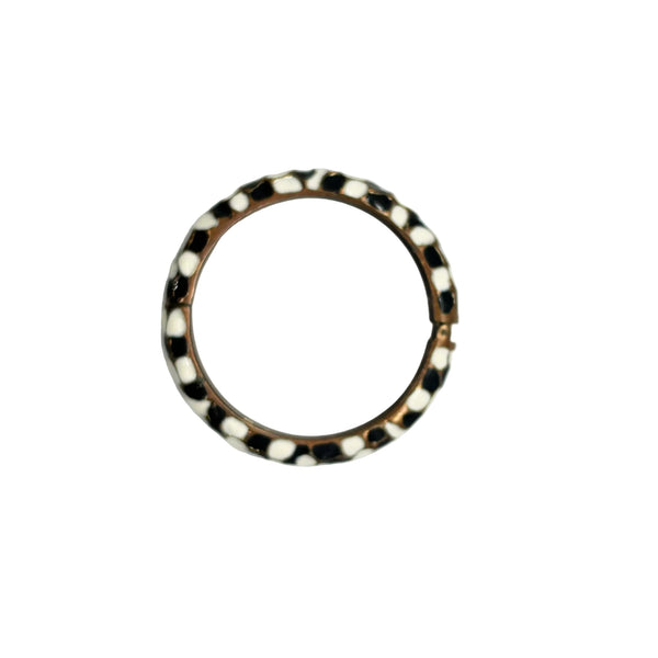 This striking hinge bangle bracelet showcases bold geometric patterns rendered in contrasting black and white enamel, accented with warm copper metalwork. The repeating abstract design creates visual interest from every angle, making it a versatile piece that complements both casual and dressed-up looks