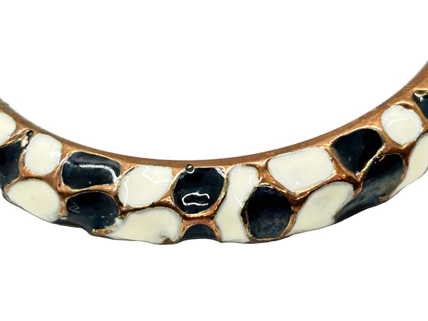 This striking hinge bangle bracelet showcases bold geometric patterns rendered in contrasting black and white enamel, accented with warm copper metalwork. The repeating abstract design creates visual interest from every angle, making it a versatile piece that complements both casual and dressed-up looks