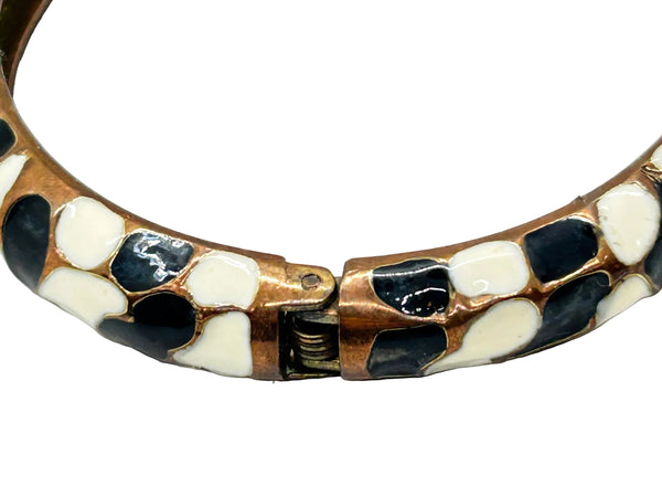 This striking hinge bangle bracelet showcases bold geometric patterns rendered in contrasting black and white enamel, accented with warm copper metalwork. The repeating abstract design creates visual interest from every angle, making it a versatile piece that complements both casual and dressed-up looks
