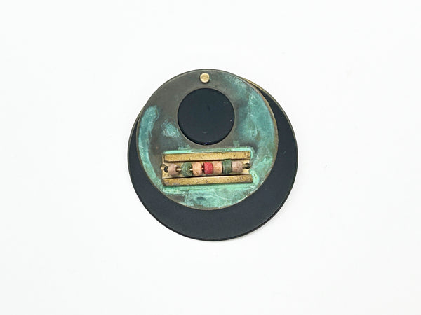 Intriguing modernist brooch with layered circular components, including a dark, possibly rubber or ebonized material, and a verdigris-patinated or painted metal plate.