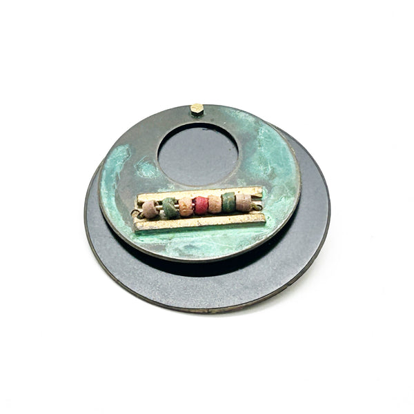 Intriguing modernist brooch with layered circular components, including a dark, possibly rubber or ebonized material, and a verdigris-patinated or painted metal plate.