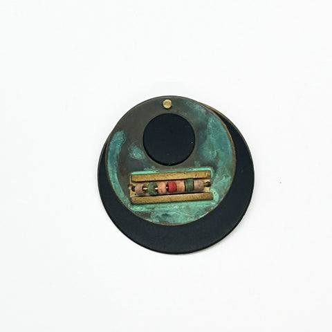Intriguing modernist brooch with layered circular components, including a dark, possibly rubber or ebonized material, and a verdigris-patinated or painted metal plate.