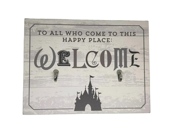 This is a Disney Parks "Welcome to All Who Come to This Happy Place" Key Ring Holder. TO THIS HAPPY PLACE: WELCOME.", featuring a silhouette of a Disney castle and two hooks, likely for hanging items like keys or leashes. It has a gray background with iconic Disney font letters.