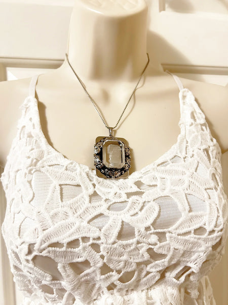 . Encased on a silver rectangular frame, this clear rectangular glass pendant is bezel set and exudes timeless charm.&nbsp;It is mounted in a silver rectangular frame adorned with a garland.&nbsp; Measuring 1.75 inches in height and 1.25 inches across, it is a substantial piece that will make a statement. 