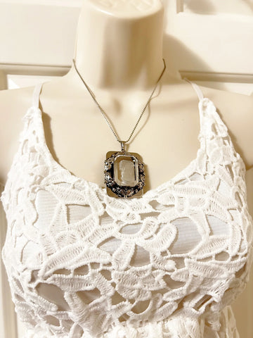 . Encased on a silver rectangular frame, this clear rectangular glass pendant is bezel set and exudes timeless charm.&nbsp;It is mounted in a silver rectangular frame adorned with a garland.&nbsp; Measuring 1.75 inches in height and 1.25 inches across, it is a substantial piece that will make a statement. 