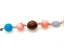 A beaded strand featuring a sequence of colorful round beads: blue, pink, brown, coral pink, lavender, and gold-toned metal links, shown against a plain white background.