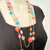 A long multi-strand statement necklace with colorful glass beads and gold-toned chain links, displayed on a mannequin wearing a black top.