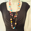 A multi-strand beaded necklace displayed on a black mannequin torso. The necklace features gold-tone chains and colorful beads in pink, orange, blue, yellow, and white.