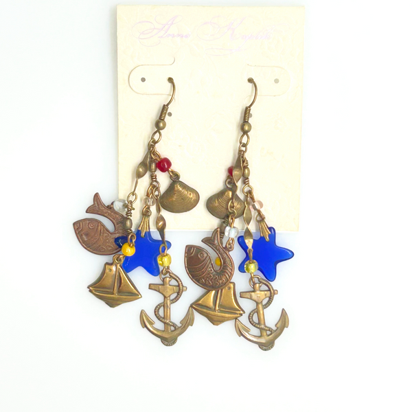 Vintage Cookie Lee nautical charm dangle earrings in antiqued brass featuring anchor, sailboat, fish, and blue star charms on a cream card