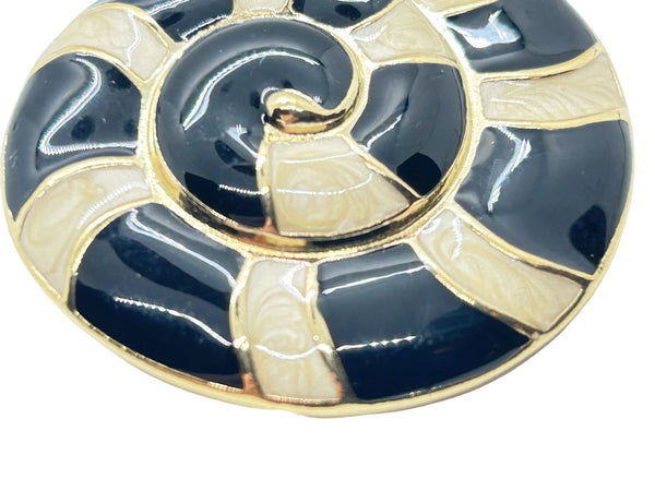 This stunning Trifari brooch captures the elegance of Art Deco design with its spiral seashell silhouette. Crafted in gold-tone metal, it features striking black enamel paired with creamy golden-sand enamel in a sophisticated moire finish.