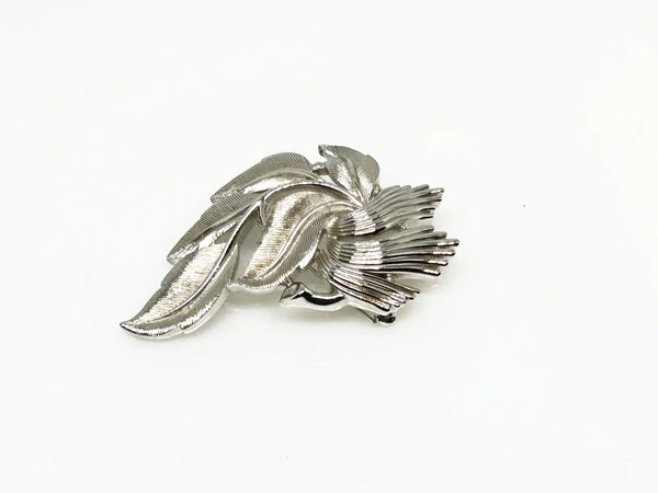 An exquisite piece of vintage jewelry, the Crown Trifari Brushed Silver tone Leaf Brooch boasts eight beautifully crafted leaves, with five showcasing brushed silver tone metal and three displaying a stylized abstract design