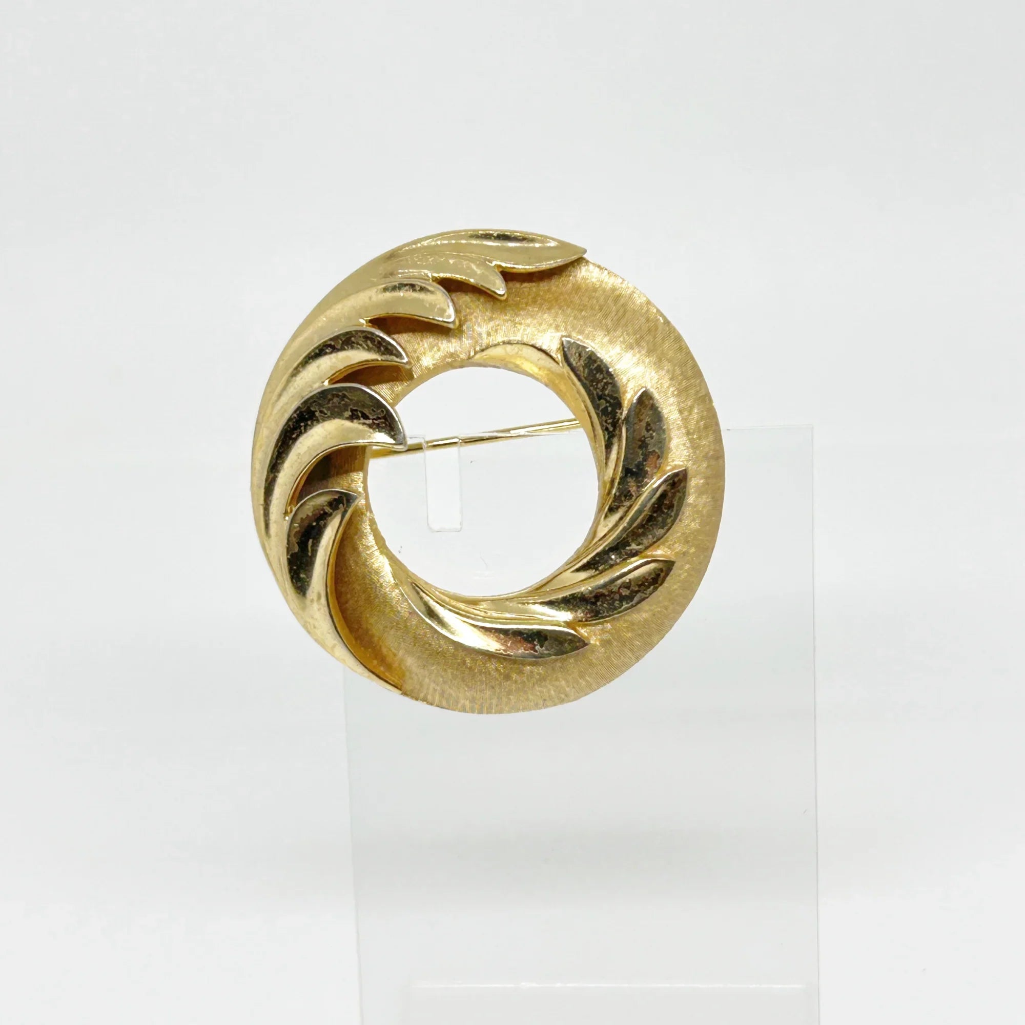 &nbsp;This Crown Trifari brooch combines smooth and textured finishes across two layers, featuring an elegant abstract wave design. A timeless addition to any collection, it’s perfect for making a lasting impression in your wardrobe. Measuring 1.75" in diameter and in excellent condition, it offers a substantial feel of quality.