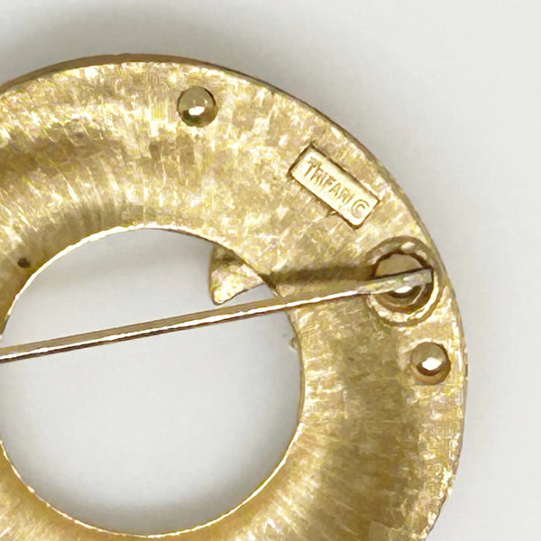 &nbsp;This Crown Trifari brooch combines smooth and textured finishes across two layers, featuring an elegant abstract wave design. A timeless addition to any collection, it’s perfect for making a lasting impression in your wardrobe. Measuring 1.75" in diameter and in excellent condition, it offers a substantial feel of quality.