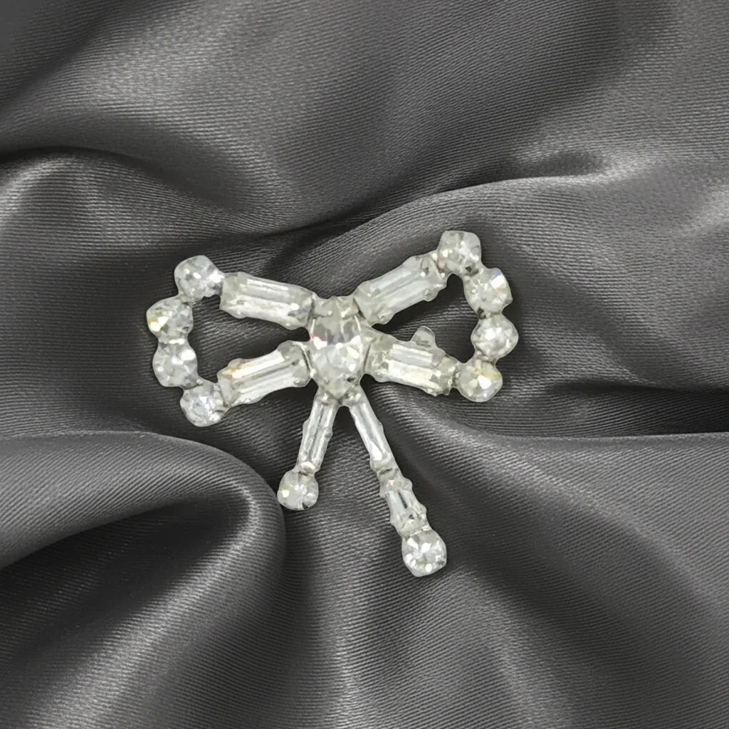 Enhance any outfit with this delicate and exquisite Tiny Rhinestone Vintage Bow Brooch. With its stunning baguette and round stones, hand-set in a sleek frame, this brooch adds a touch of glamour that surpasses what the camera can capture