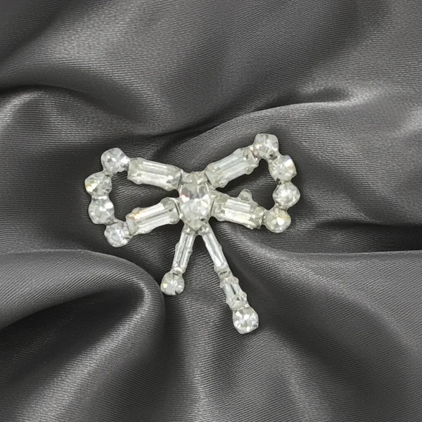 Enhance any outfit with this delicate and exquisite Tiny Rhinestone Vintage Bow Brooch. With its stunning baguette and round stones, hand-set in a sleek frame, this brooch adds a touch of glamour that surpasses what the camera can capture