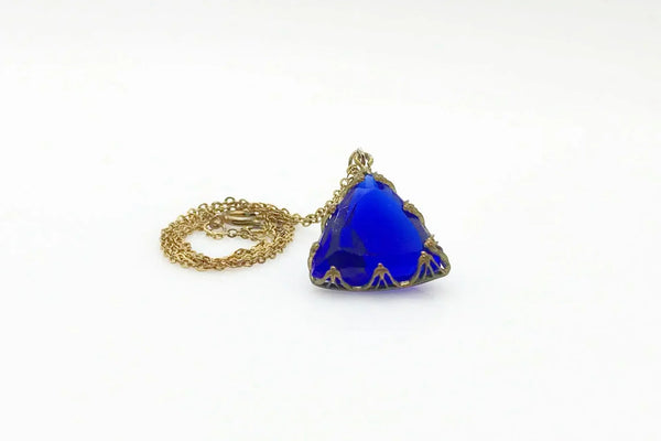 This extraordinary Art Deco pendant necklace is a true collector's treasure, featuring a stunning triangular faceted cobalt blue glass stone that shifts between rich cobalt and mesmerizing violet tones depending on the light.