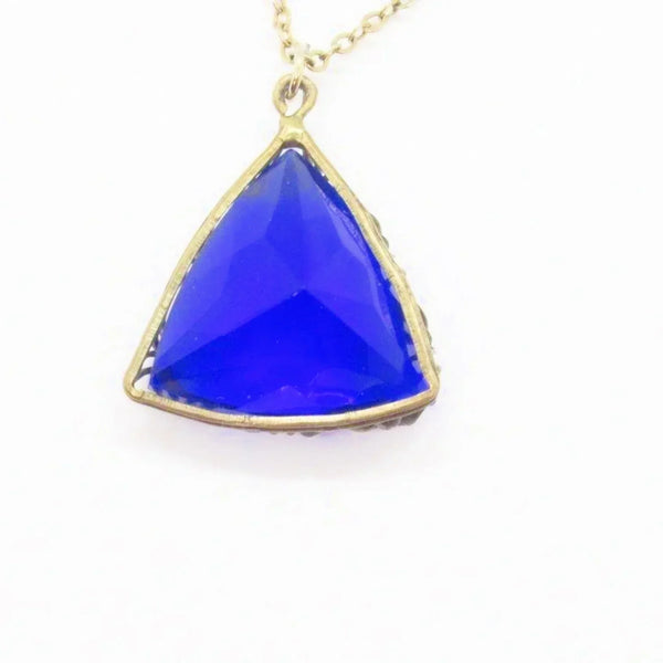 This extraordinary Art Deco pendant necklace is a true collector's treasure, featuring a stunning triangular faceted cobalt blue glass stone that shifts between rich cobalt and mesmerizing violet tones depending on the light.